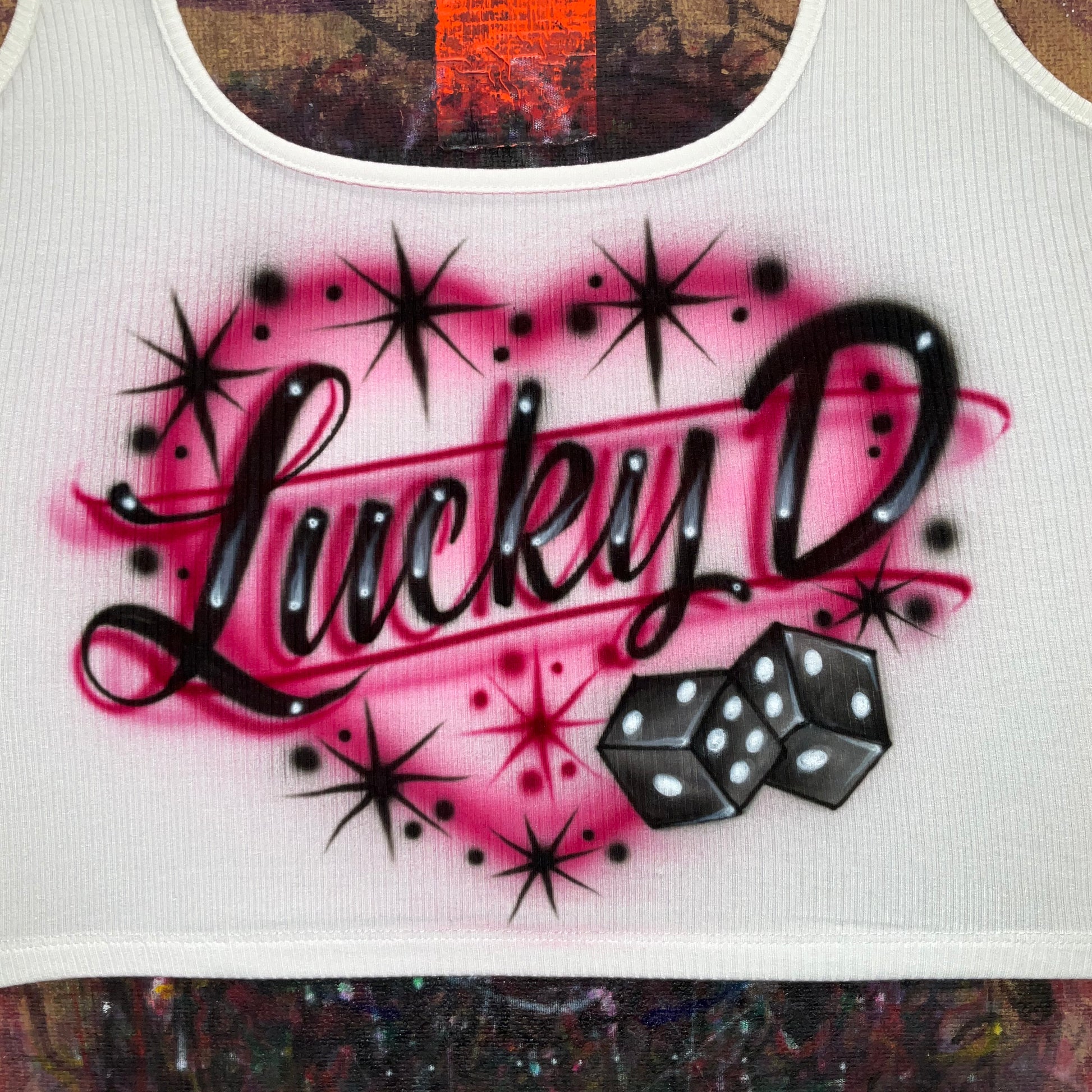 Hand airbrushed Lucky dice design with glossy black dice, fuchsia glow, and black starburst accents on white apparel.
