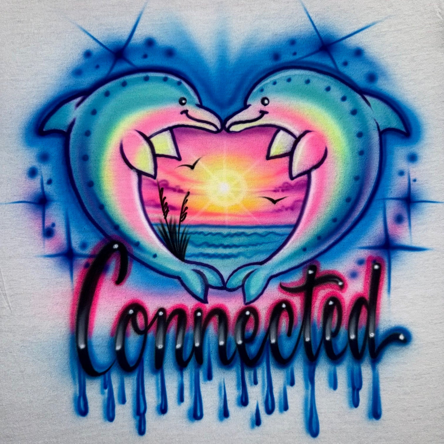 Airbrushed Connected shirt with drippy letters and twin dolphins forming a heart around a glowing sunset beach, fan-inspired handmade design