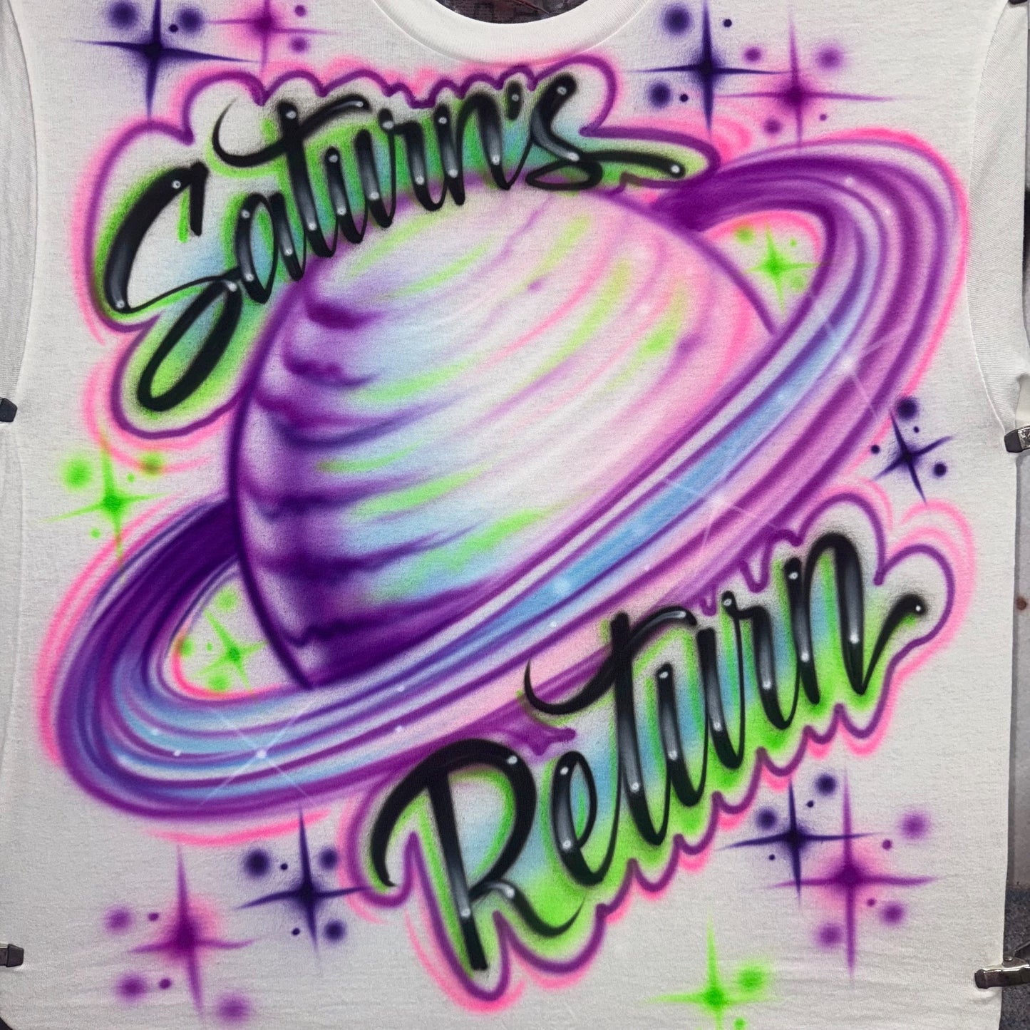 Airbrushed Saturn’s Return full-front shirt with neon purple, pink, green, and blue planet Saturn and sparkles, fan-inspired cosmic design