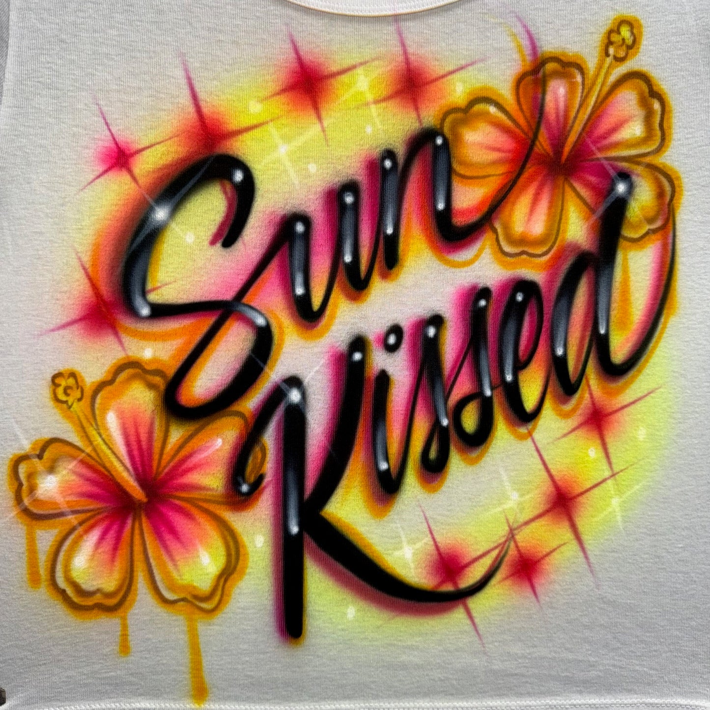 Sun Kissed hand airbrushed hibiscus heart design with glowing summer colors and starburst accents on cotton shirt