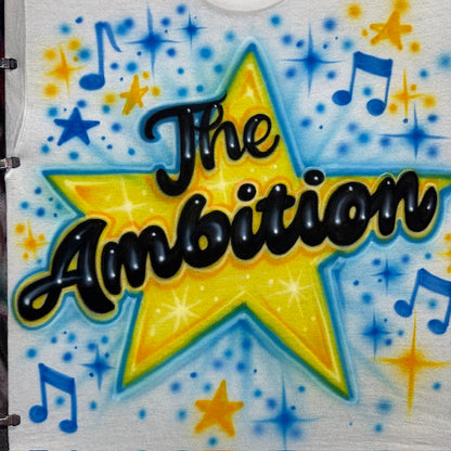 Hand-airbrushed The Ambition shirt with large yellow star, black script lettering, blue music notes and colorful starburst accents